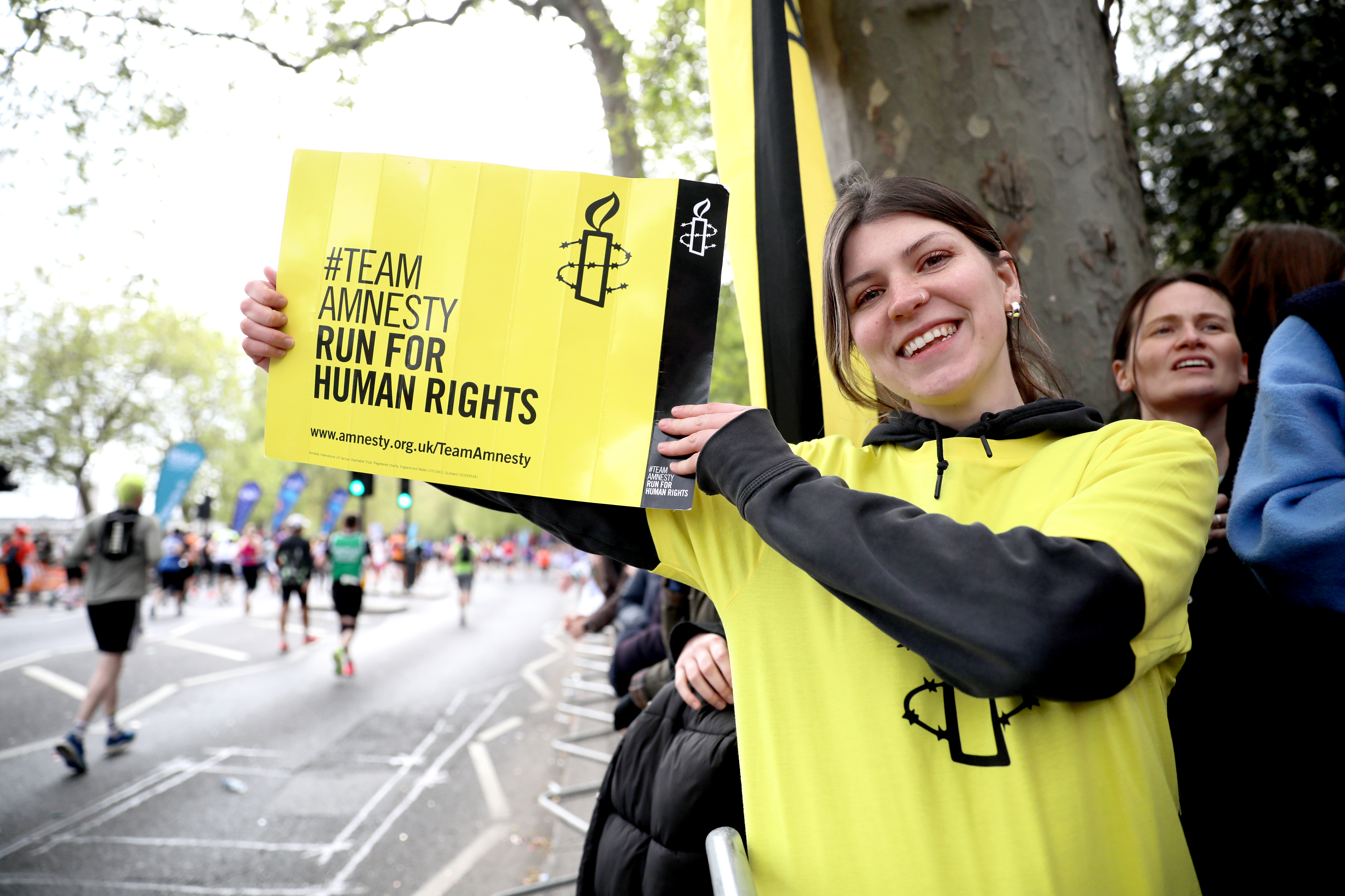 Amnesty Supporter Holding Placard in support of Team Amnesty at the London Marathon in a London Street