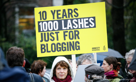 "A person holds an Anmnesty placard that reads: 10 years, 1000 lashes, just for blogging"