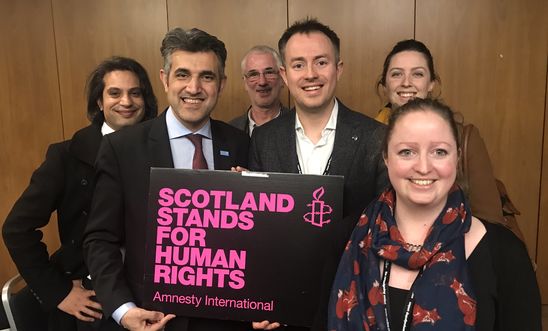 A group of people hold up an Amnesty International placard that says 'Scotland stands for human rights'