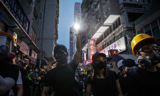 Anti-government protesters wearing gas masks and holding placards march on Hong Kong at dusk