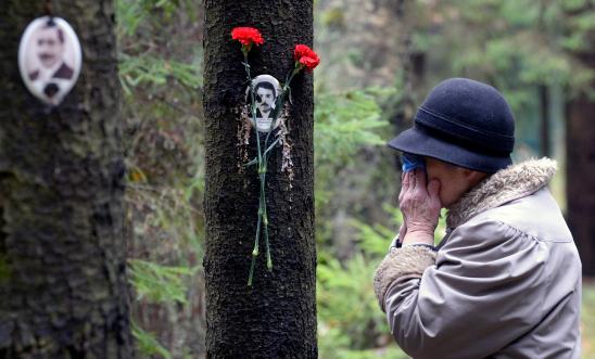 A woman reacts next to a portrait of a victim of Soviet dictator Joseph Stalin's purges at the memorial, where the victims were buried in the woods on the outskirts of Saint-Petersburg, on October 30, 2017.