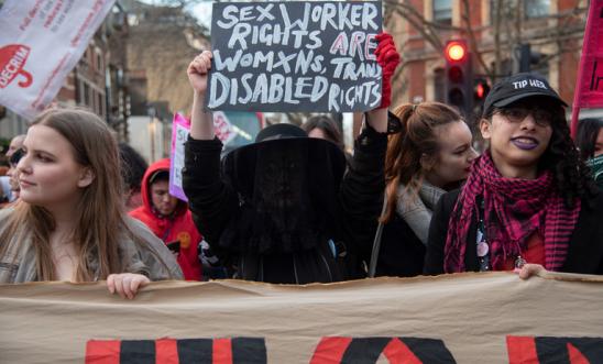 Three women march at a demonstration, with the central figure holding a placard saying 'Sex worker rights are women's rights, trans rights and disabled rights' 