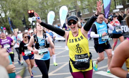 Amnesty London marathon runner smiling with hands in the air while runners for other charities run in the background
