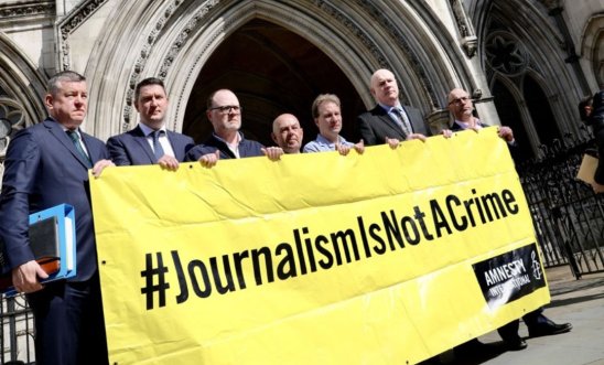 Journalists stood in from the Royal Courts of Justice holding a banner reading journalism is not a crime