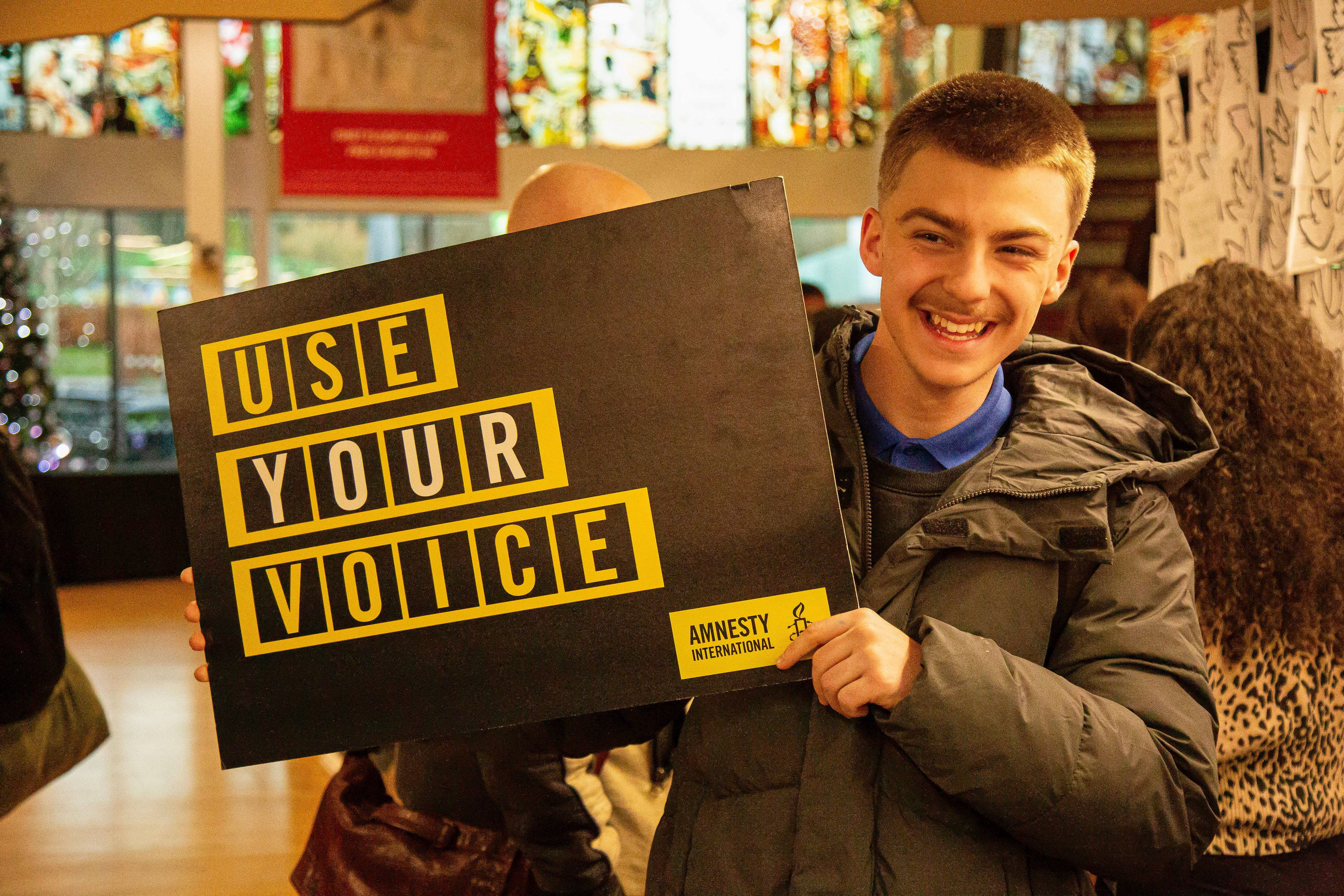"person smiling holding a placard that reads: use your voice"