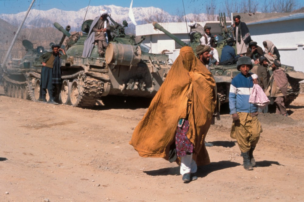 Afghan woman and boy walk by a tank in Kabul, 2004