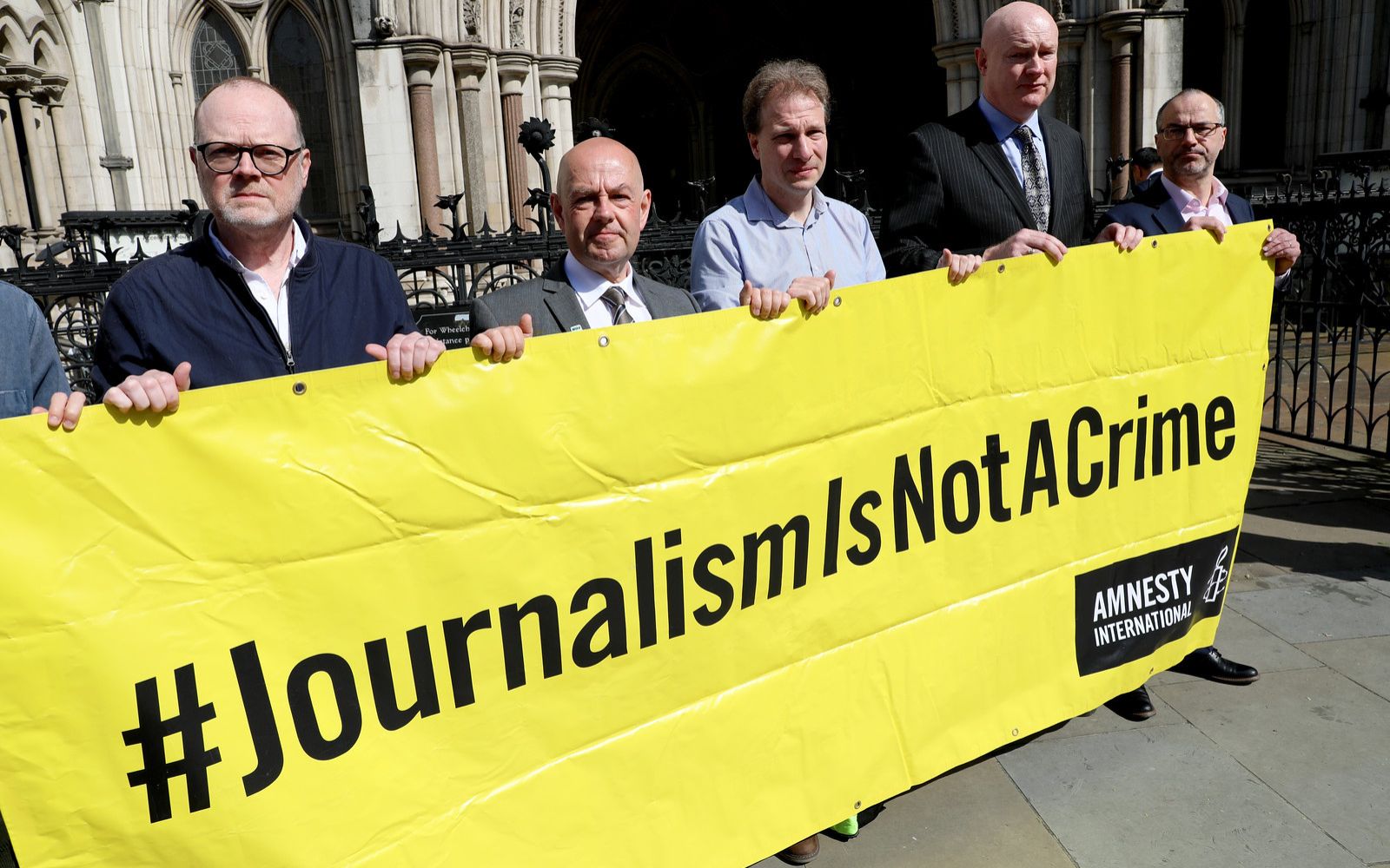 Barry McCaffrey and Trevor Birney standing with others outside the courts holding a banner that says journalism is not a crime. Barry McCaffrey and Trevor Birney standing with others outside the courts holding a banner that says journalism is not a crime.