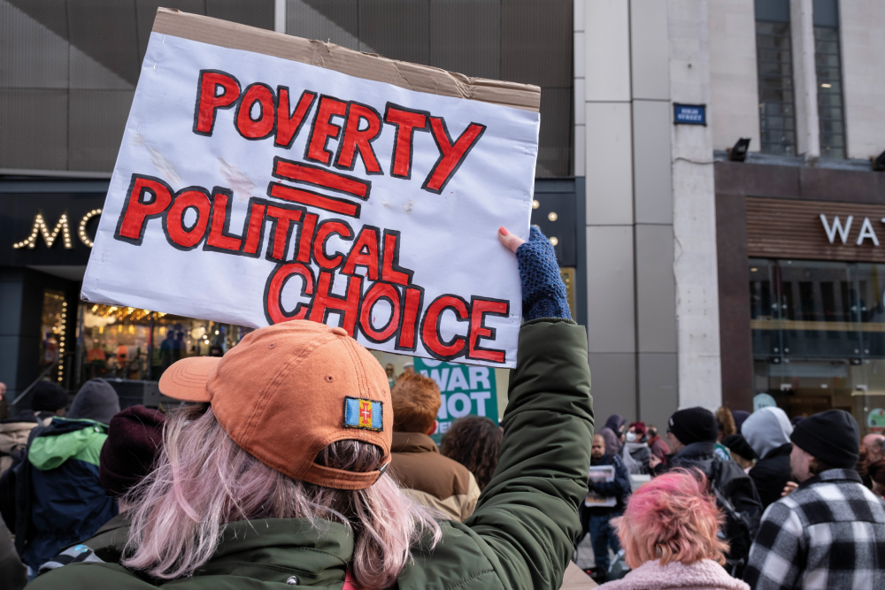 Person holding up a sign in a rally that says Poverty Equals Political Choice.