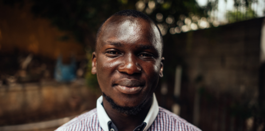 Imoleayo stands and smiles at camera outside some buildings