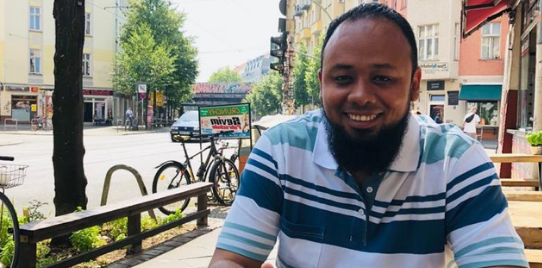 Mohamed smiles looking at camera sitting at cafe outside