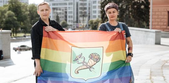 Anna and Vira stand outside and hold a rainbow LGBTI+ flag