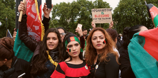 Women in London at a protest for Afghanistan dressed in country colours and holding the flag, Text reads Afghanistan. Stand with women and girls - Photo by Ehimetalor Akhere Unuabona