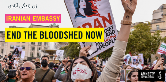 In the front, a woman with a facemark saying "AZADI" and holding her arm raised with an open palm, in her palm, the word "FREEDOM". In Farsi it reads "woman life freedom". A banner reads "iranian embasys" and "end the bloodshed now". The amnesy logo in black and white are on the right bottom corner. 