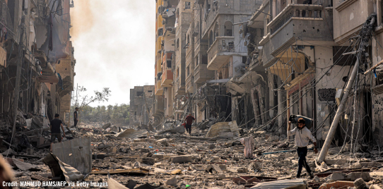 A man carries a propane gas cylinder on his back while walking through debris and destruction littering a street in the Jabalia camp for Palestinian refugees in Gaza City on October 11, 2023.