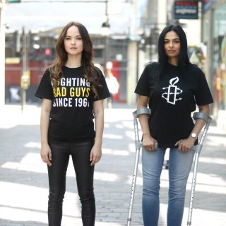 Two people wearing Amnesty branded t-shirts, one is standing one crutches