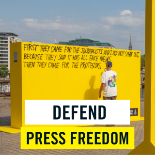 Photo of a man writing a passage about press freedom, with an image banner saying Defend Press Freedom
