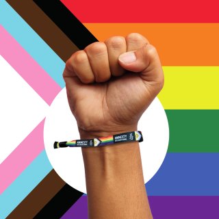Pride Flag with a hand in the front wearing an Amnesty Rainbow Bracelet