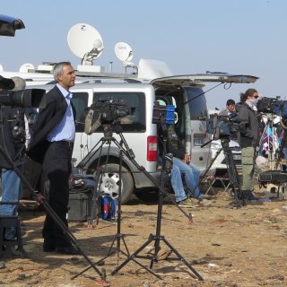 Man standing in front of a news crew with cameras and outside a news van