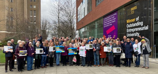 Amnesty Central England Network members standing outside a building in solidarity, holding placards. Amnesty Central England Network members standing outside a building in solidarity, holding placards.