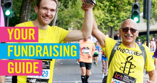 Two Amnesty supporters in Amnesty shirts holding hands up after completing a marathon event with title of 'Your Fundraising Guide'