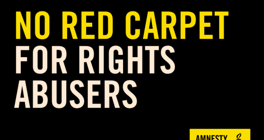 A black placard that reads No Red Carpet for Rights Abusers with an Amnesty logo in the bottom-right corner