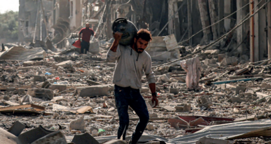 A man carries a propane gas cylinder in the Jabalia camp for Palestinian refugees in Gaza City on 11 October, 2023, amid destruction caused by Israeli air strikes