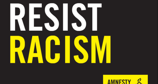 A black placard that reads 'Resist Racism' with an Amnesty logo in the bottom-right corner