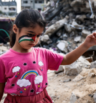 A young girl with a Palestinian flag face-painting walking on the rubble 