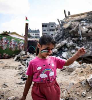 A young girl with a Palestinian flag face-painting walking on the rubble 