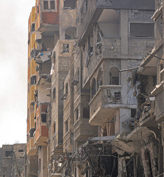 A man carries a propane gas cylinder on his back while walking through debris and destruction littering a street in the Jabalia camp for Palestinian refugees in Gaza City on October 11, 2023.
