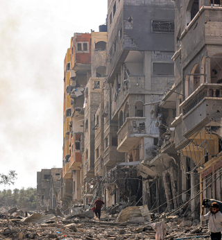 A man carries a propane gas cylinder on his back while walking through debris and destruction littering a street in the Jabalia camp for Palestinian refugees in Gaza City on October 11, 2023.