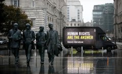 Image shows 4 statues and a black van in the background with text in yellow saying "Human Rights Are the Answer"