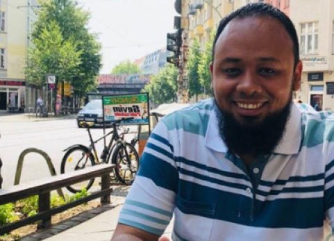 Mohamed smiles at camera outside cafe