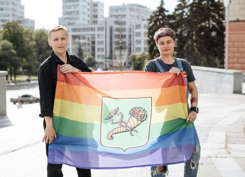 Anna and Vira stand outside and hold a rainbow LGBTI+ flag