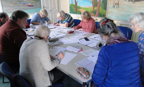 People sitting round a table writing letters People sitting round a table writing letters
