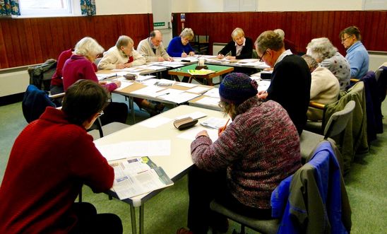 People sitting  round a table writing letters