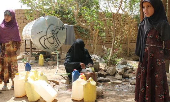 Two Yemeni children and a woman in Magash fetch water from a freestanding tank