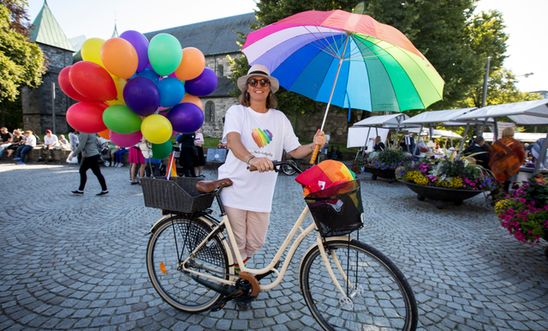A cyclist with rainbow balloons and umbrella, at Pride.