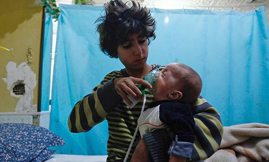 A Syrian boy holds an oxygen mask over the face of an infant at a make-shift hospital following a reported gas attack on the rebel-held besieged town of Douma in the eastern Ghouta region, 22 January 2018.