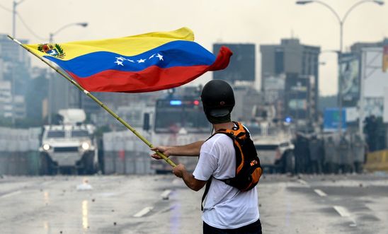 A Venezuelan opposition demonstrator waves a flag at the riot police