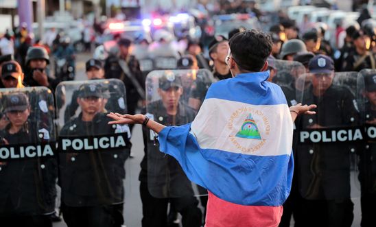 An anti-government protester wearing a national flag shouts slogans in front of a line of riot police during a protest against Nicaraguan President Ortega's government in Managua