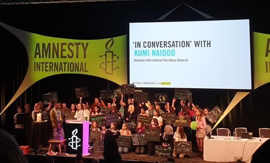 Image shows climate activists on stage at the Amnesty AGM with Kumi Naidoo