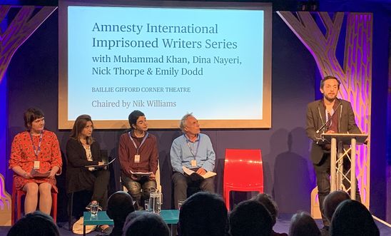 Image shows a man reading at a lectern whilst four people sit on a stage 