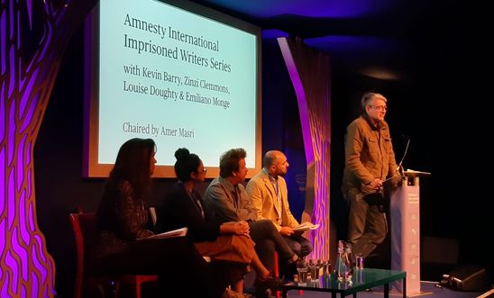 Image shows four people listening to a man at a lectern Image shows four people listening to a man at a lectern