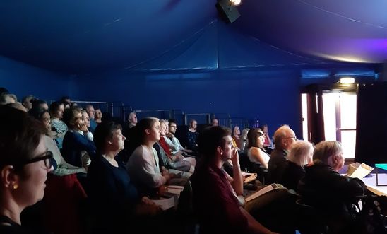 Image shows an audience in a darkened theatre Image shows an audience in a darkened theatre