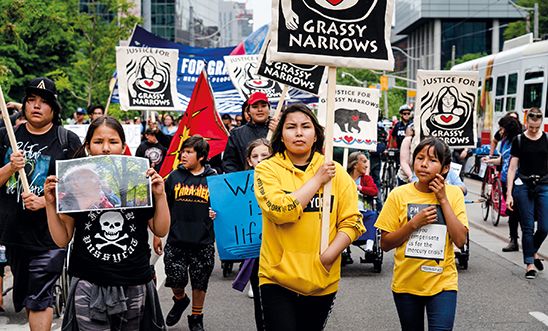 Children marching in the street carrying 'Justice for grassy narrows' placards
