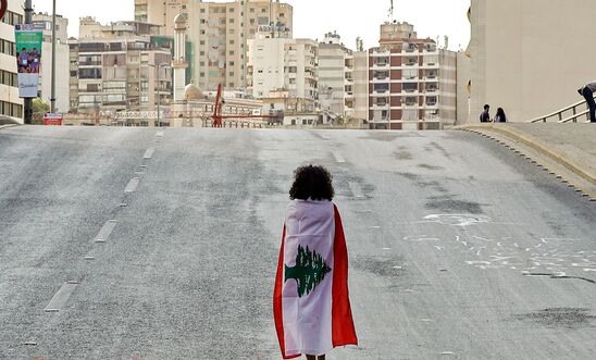 A Lebanese woman protester walks draped in a national flag along the Fuad Chehab avenue, near the Martyrs' Square, in the centre of the capital Beirut on October 29, 2019 on the 13th day of anti-government protests. 