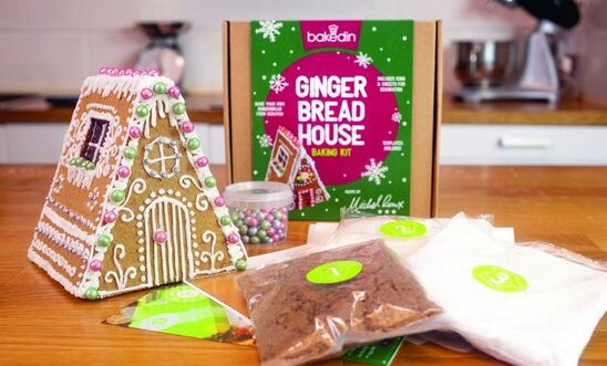 On a kitchen counter is the contents of a gingerbread house kit, including a completed gingerbread house, ingredients and colourful box On a kitchen counter is the contents of a gingerbread house kit, including a completed gingerbread house, ingredients and colourful box
