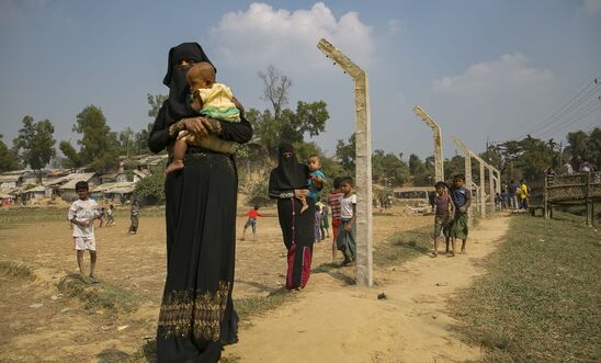 Rohingya refugees walk near a fence that is being constructed around the refugee camp on December 11, 2019 Rohingya refugees walk near a fence that is being constructed around the refugee camp on December 11, 2019