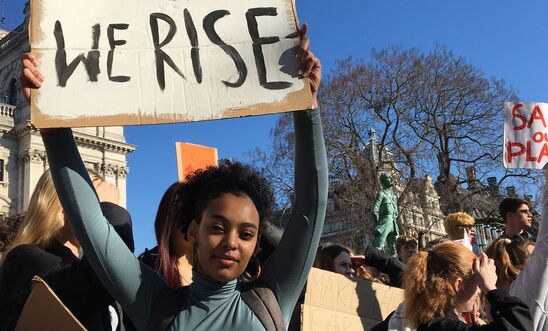 Young people hold up protest signs that read "We rise"